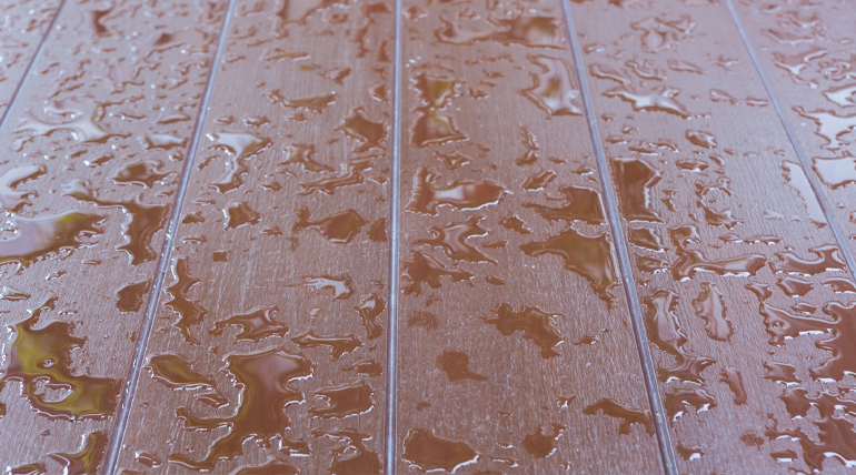 Close-up of a wooden deck with scattered raindrops reflecting light.