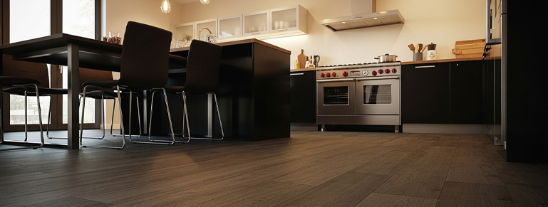 Modern kitchen with dark cabinets, stainless steel appliances, wood flooring, and a central island with dining chairs under warm pendant lighting.
